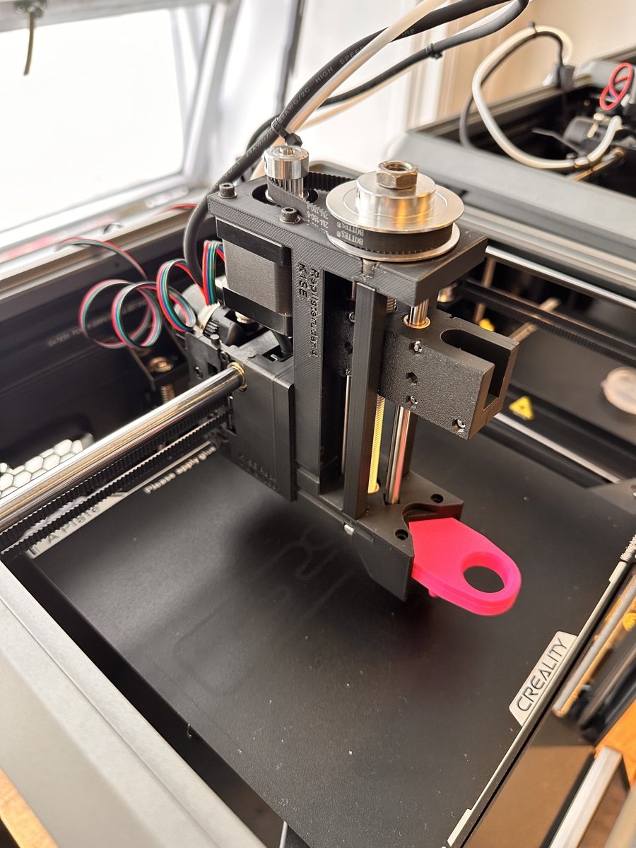 The syringe pump mounted on the printer, showing its motor, belt, and pulley, with a pink honing tool attached below