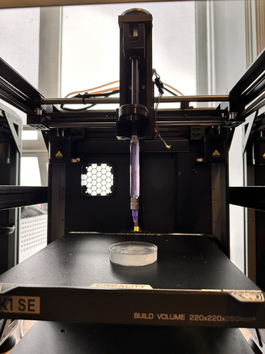Custom syringe extruder mounted on the printer, positioned above a petri dish of hydrogel