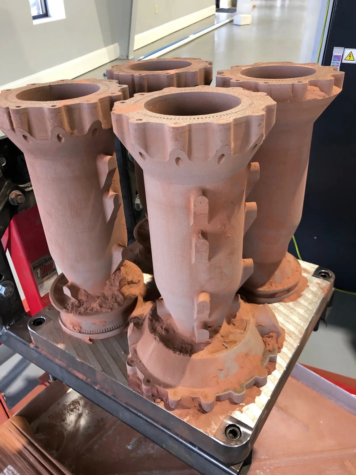 Four copper-colored 3D-printed rocket combustion chambers standing on a build plate.