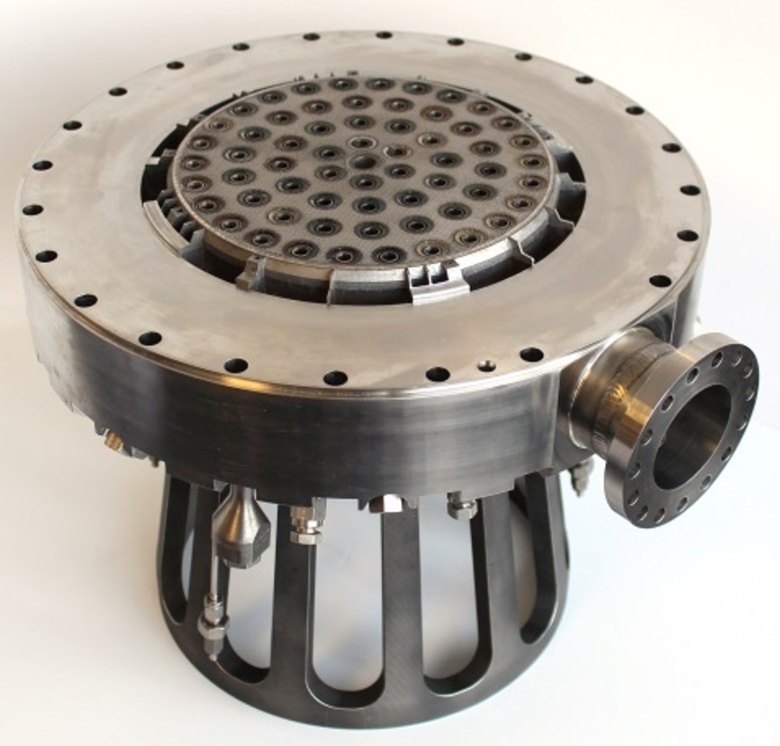 A large additively manufactured injector with a perforated face plate and bolted flange, mounted on a slotted support stand.