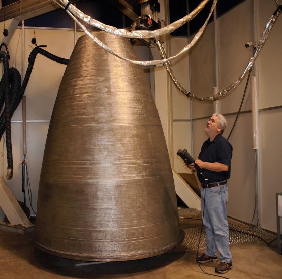 A large additively manufactured nozzle in a test facility, taller than the engineer standing beside it.