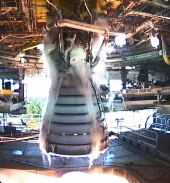 A rocket engine firing on a test stand, vapor streaming down around its nozzle.
