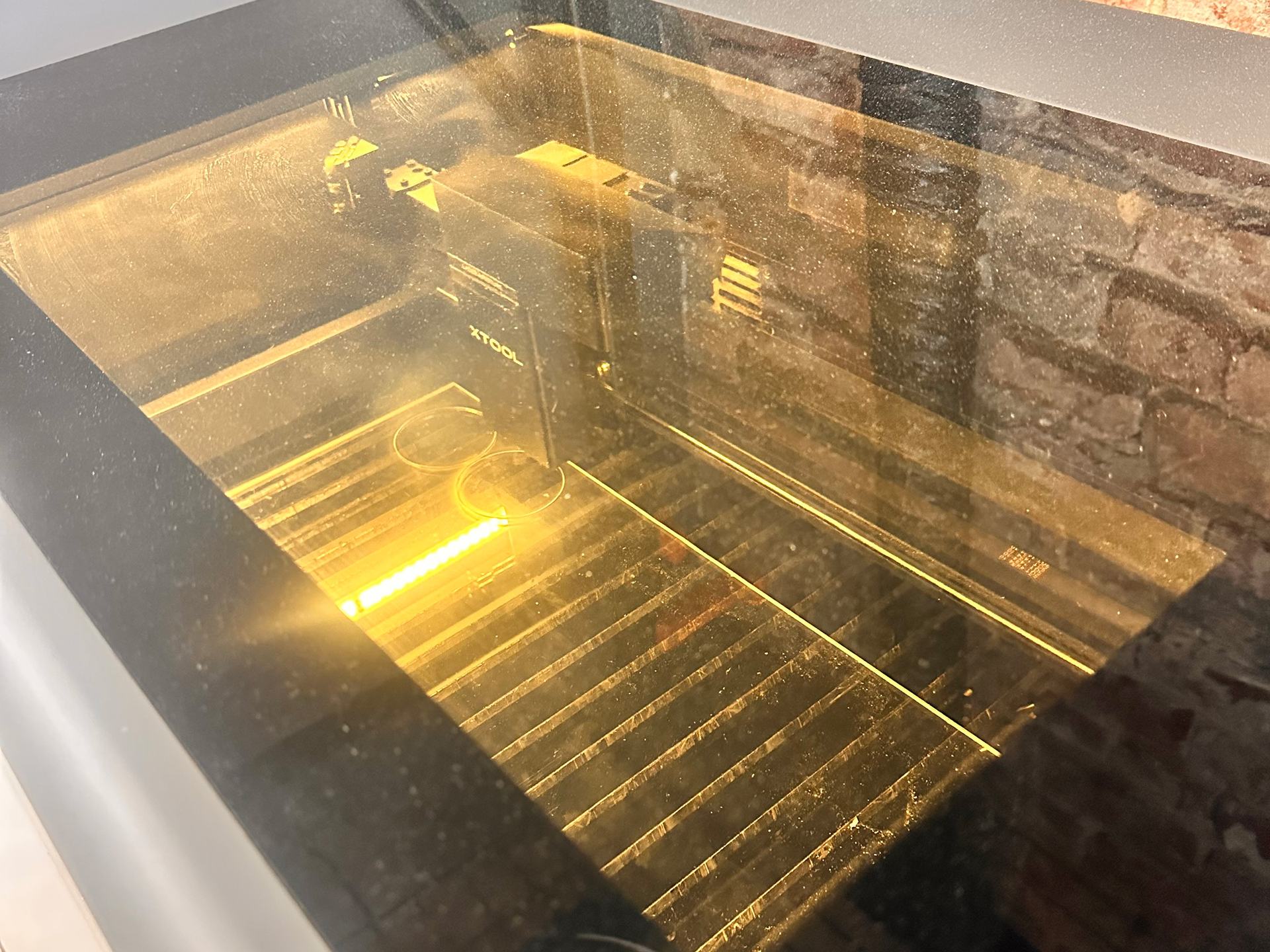 Looking through the tinted lid of an xTool laser cutter at its bed, with round acrylic cut-outs